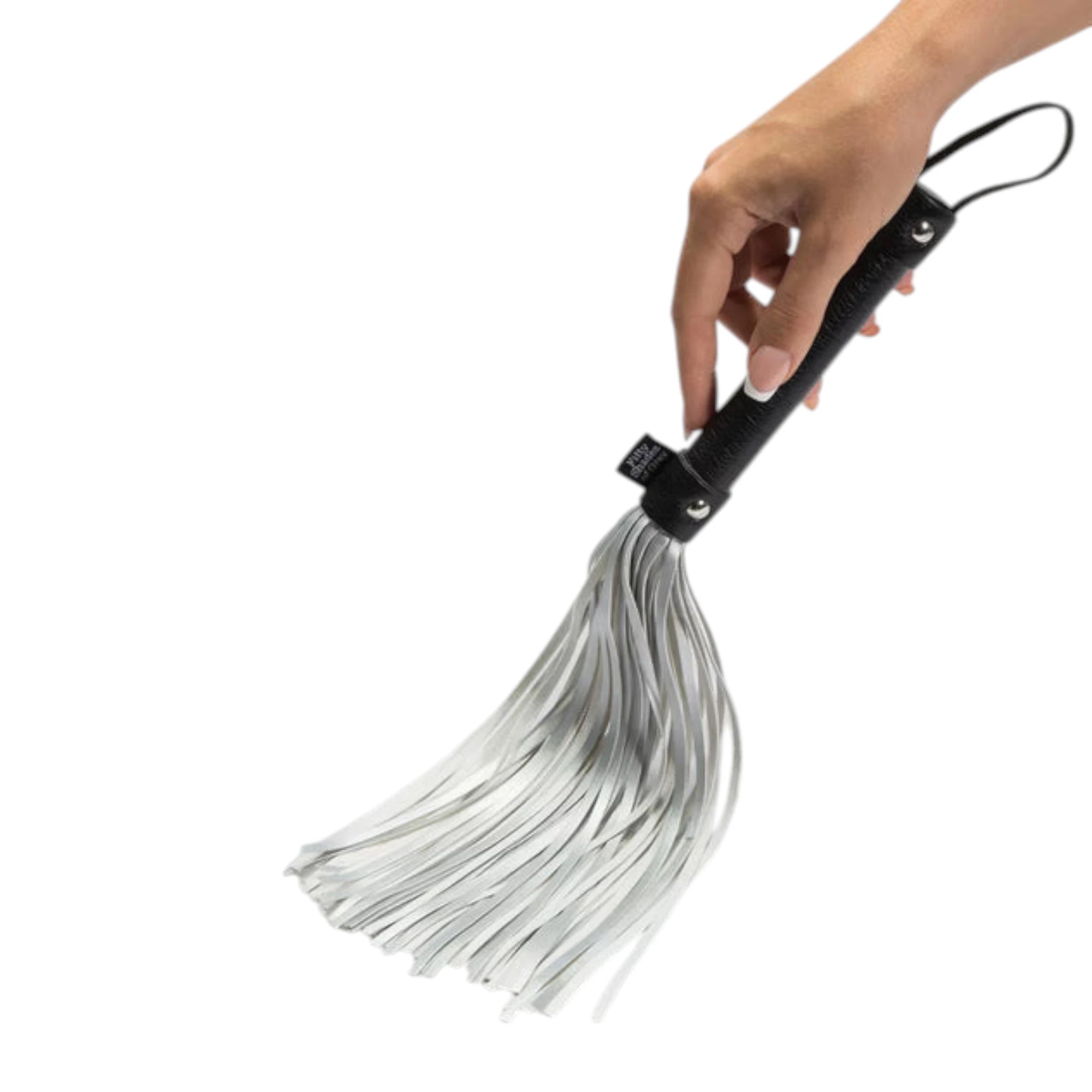 Fifty Shades of Grey Please, Sir black flogger held in hand displaying black textured handle with metal rivets, cascading white and grey leather strands in motion, wrist loop, and professional grip against white background