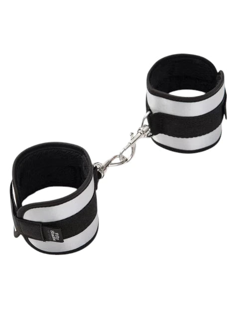 Fifty Shades of Grey Totally His soft handcuffs shown as connected pair from angled perspective displaying black neoprene lining, silver metallic exterior panels, velcro fastening straps, metal chain connector with D-rings, and Fifty Shades of Grey branding on cuff against white background