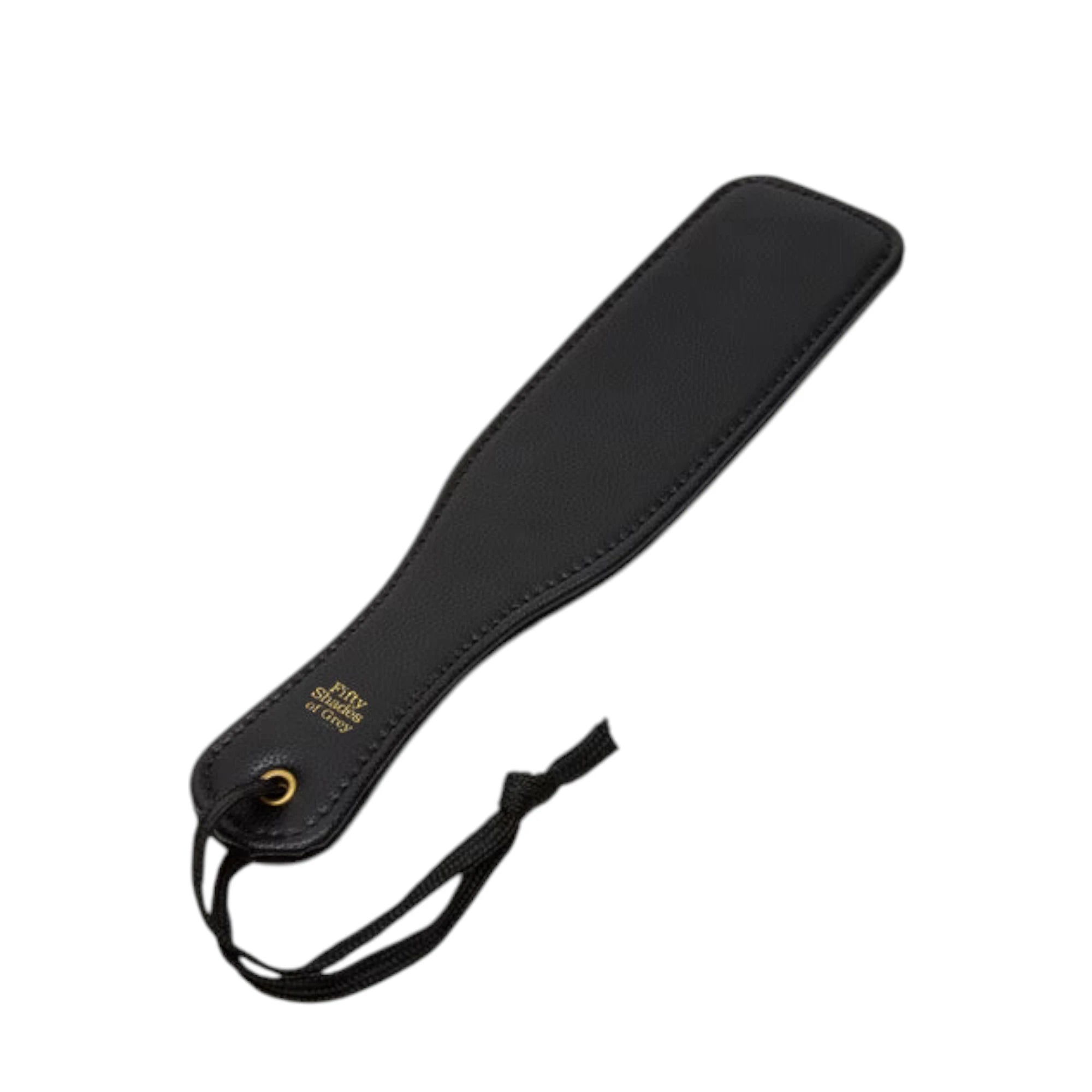 Fifty Shades of Grey Bound to You faux leather small spanking paddle in black shown from angle displaying flat paddle head with stitched edging, gold Fifty Shades of Grey branding near handle, wrist strap with gold grommet, and smooth textured surface against white background