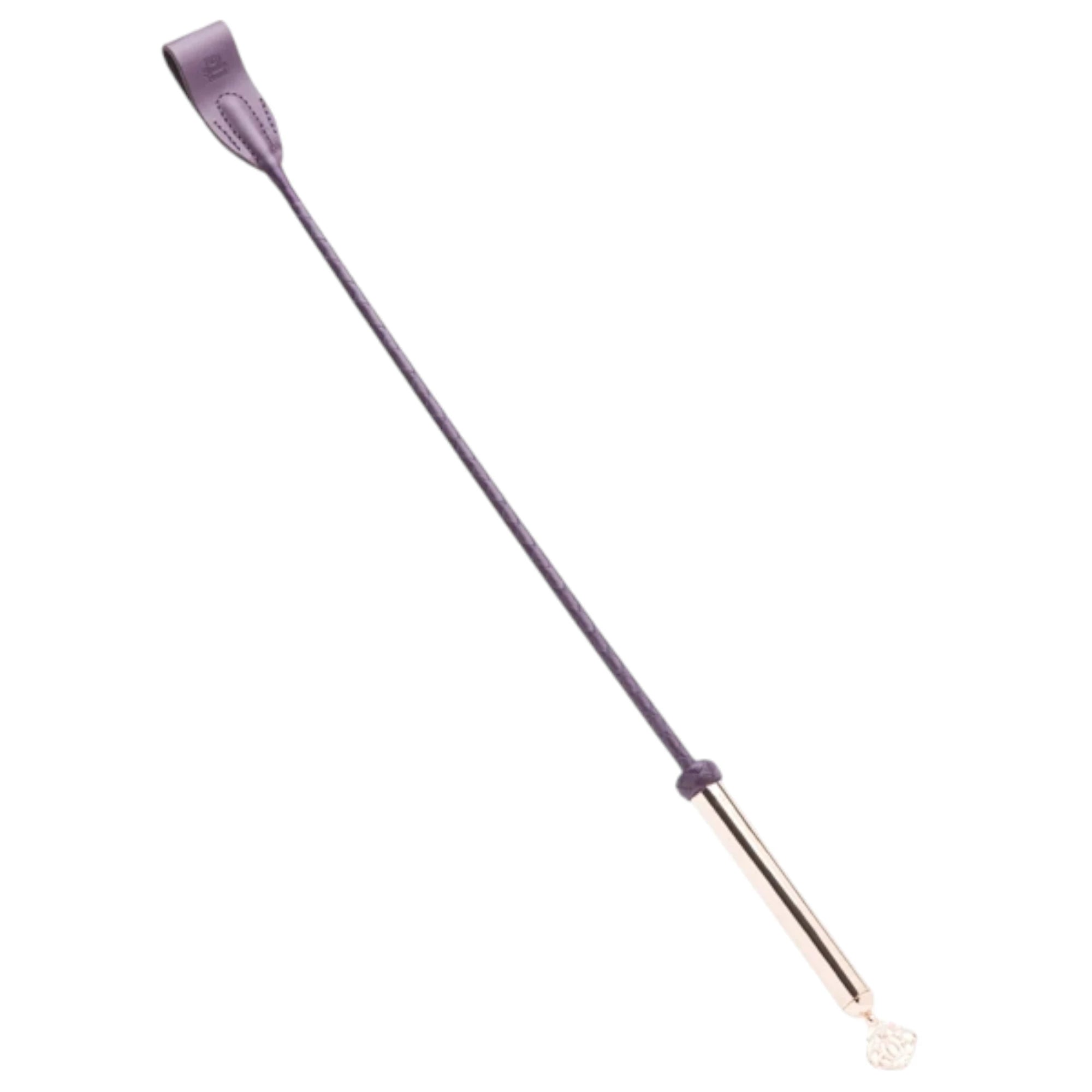 Fifty Shades Freed Cherished Collection riding crop shown at an angle, featuring a purple stitched paddle tip, slim purple shaft and a rose-gold handle with a decorative key charm at the end against a white background.