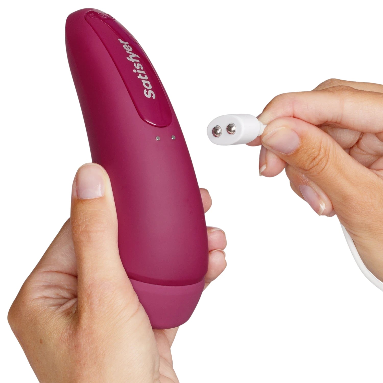The Satisfyer Curvy 1+ clitoral suction vibrator in burgundy silicone shown held in hands with a white magnetic charging cable positioned near the charging contacts, against a plain white background
