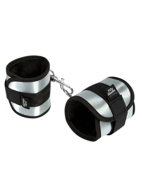 Fifty Shades of Grey Totally His soft handcuffs shown as pair displayed flat with black neoprene lining, silver metallic exterior panels, black velcro fastening straps, and attached metal D-ring against white background