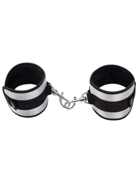 Fifty Shades of Grey Totally His soft handcuffs shown as connected pair displaying black neoprene lining, silver metallic exterior panels, velcro fastening straps, and metal chain connector with D-rings against white background