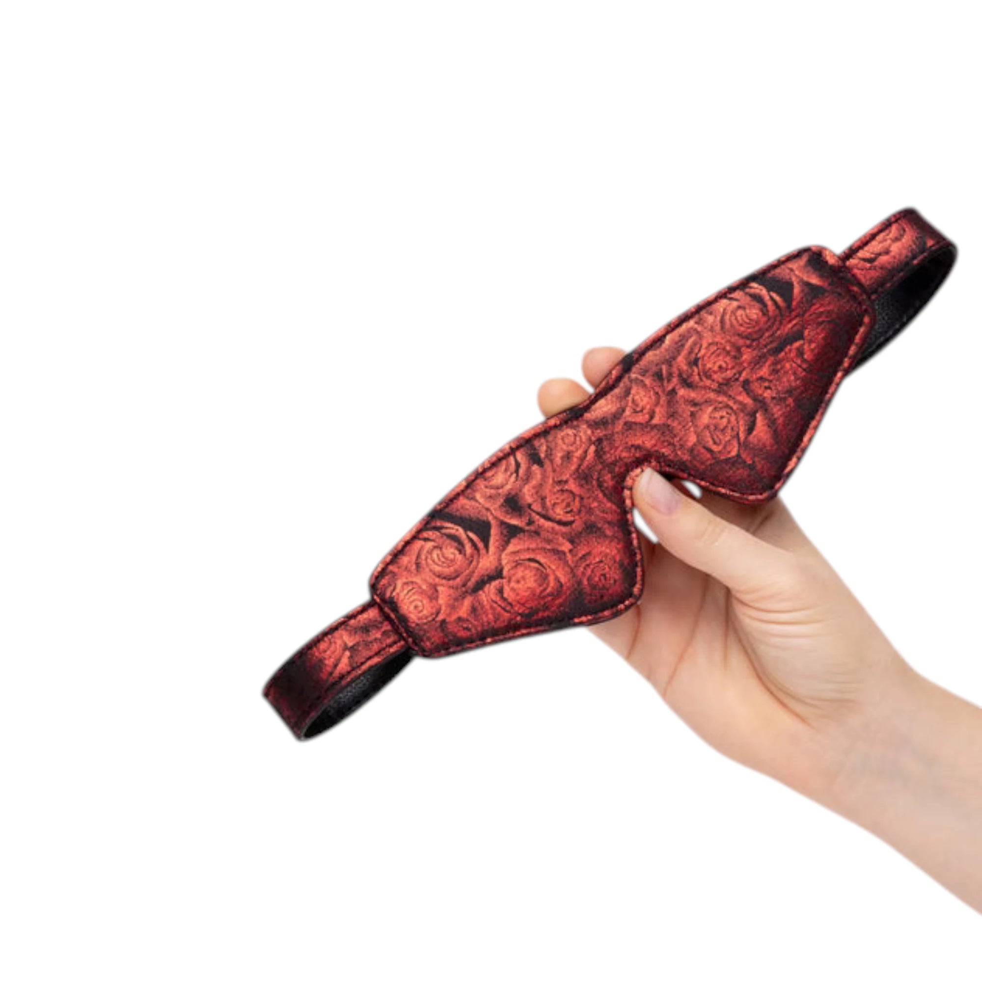 Fifty Shades of Grey Sweet Anticipation reversible faux leather blindfold in burgundy red held in hand displaying rose damask pattern, padded eye cups, adjustable fabric straps, and smooth faux leather finish against white background