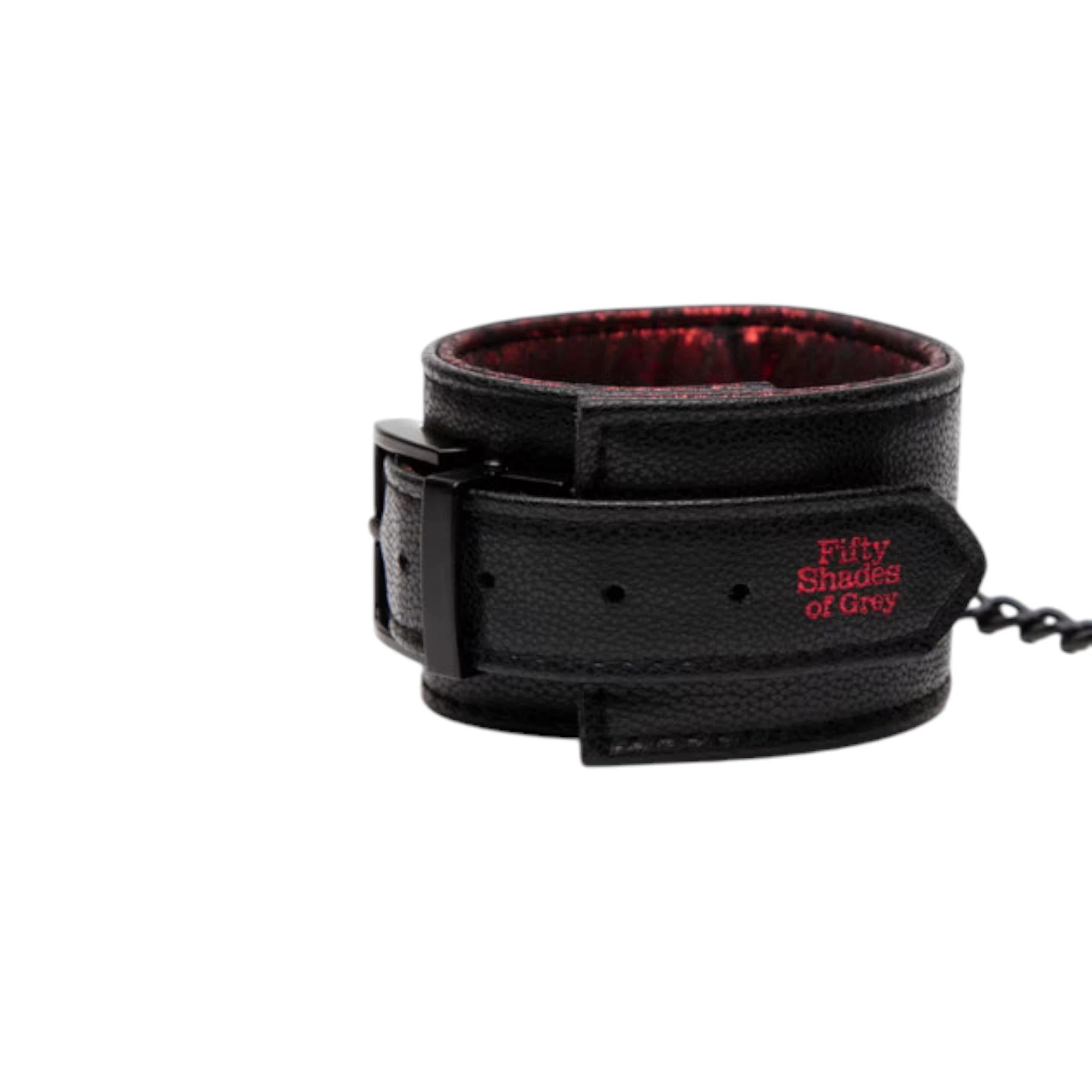 Fifty Shades of Grey Sweet Anticipation reversible faux leather wrist cuff shown close up displaying black textured exterior, red jacquard lining, adjustable buckle strap, red Fifty Shades of Grey branding, and connecting chain against white background