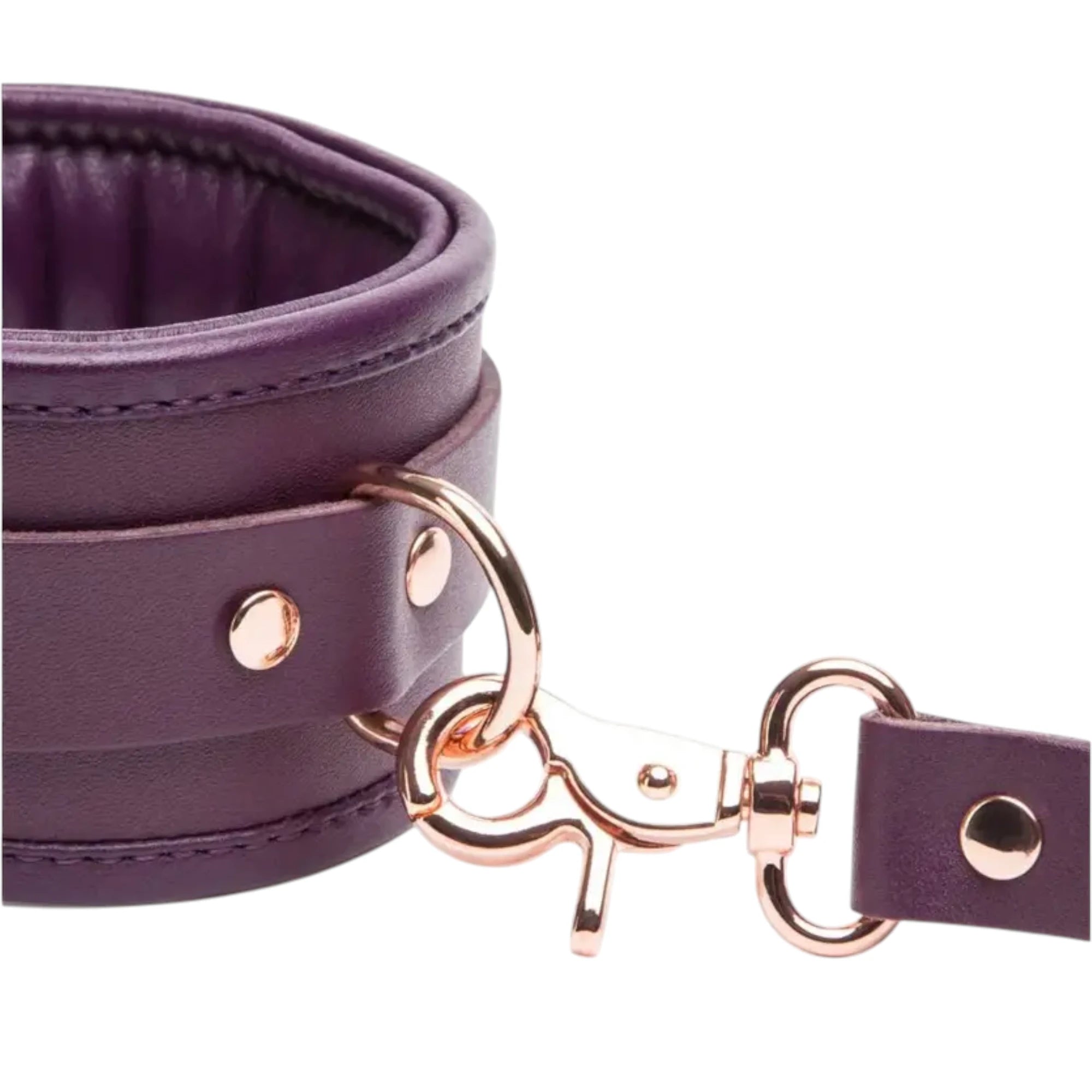Close-up of the Fifty Shades Freed Cherished Collection leather ankle cuff hardware, showing the purple padded cuff with rose-gold rivets, D-ring attachment and the connecting strap clip against a white background