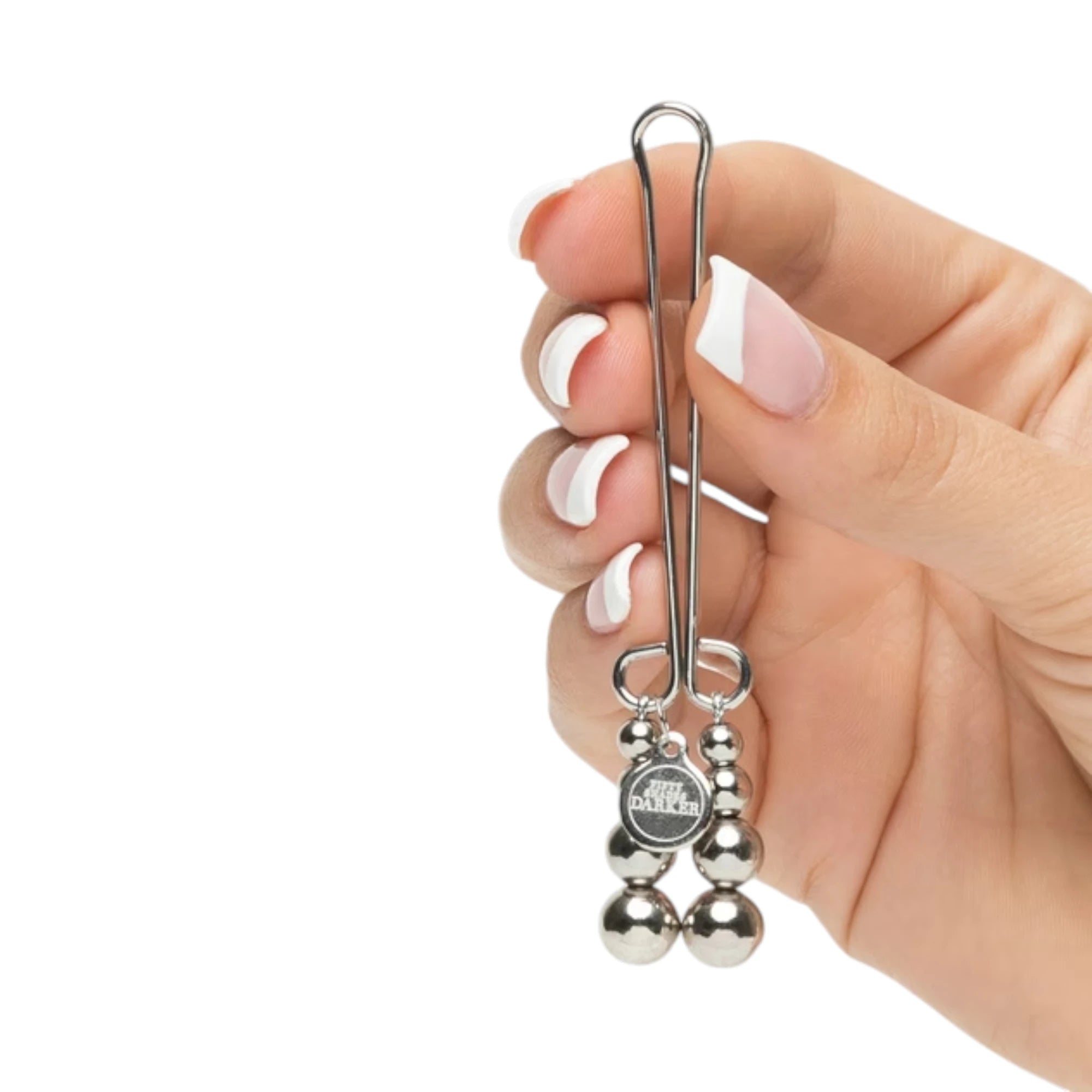 Fifty Shades Darker Just Sensation beaded clitoral clamp shown held in a hand for size reference, featuring a silver metal clamp with loop handle and two dangling strands of graduated metal beads with a small branded charm against a white background.
