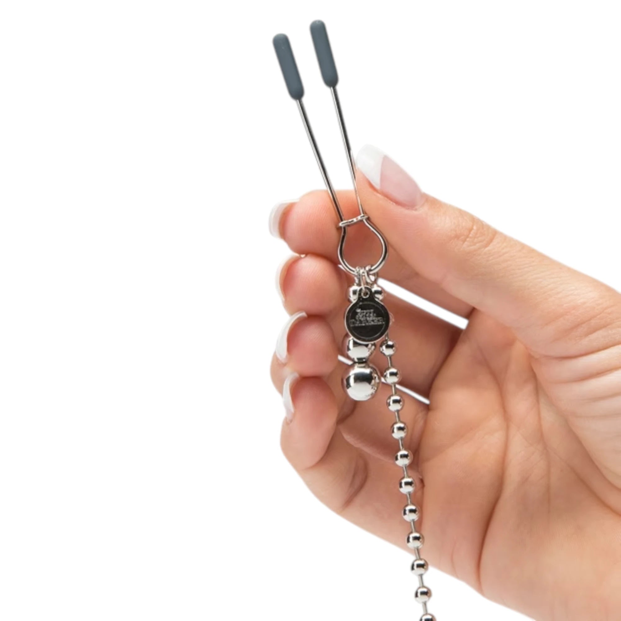 Fifty Shades Darker At My Mercy chained nipple clamps shown held in a hand for size reference, featuring a silver metal clamp with grey rubber tips, dangling bead weights, branded charm and the beaded chain connector against a white background