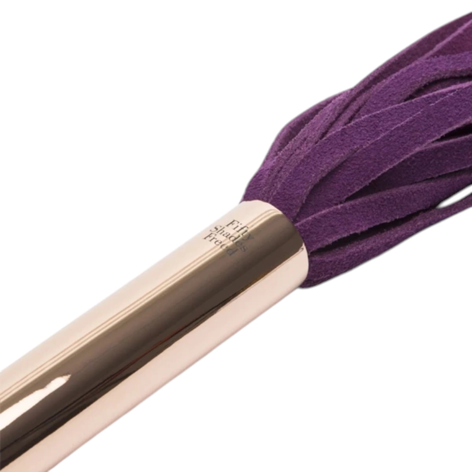 Close-up of the Fifty Shades Freed Cherished Collection flogger handle, showing the rose-gold metal grip with Fifty Shades Freed branding and the purple faux-leather tails attached at the top against a white background