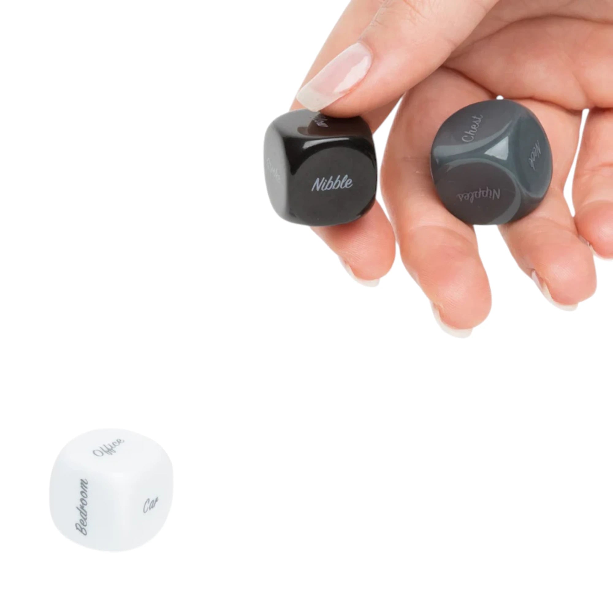 Fifty Shades of Grey Play Nice kinky dice for couples held in hand displaying two black engraved dice with text options including Nibble and Cuddle, with white die visible below showing Bedroom and Cat text against white background