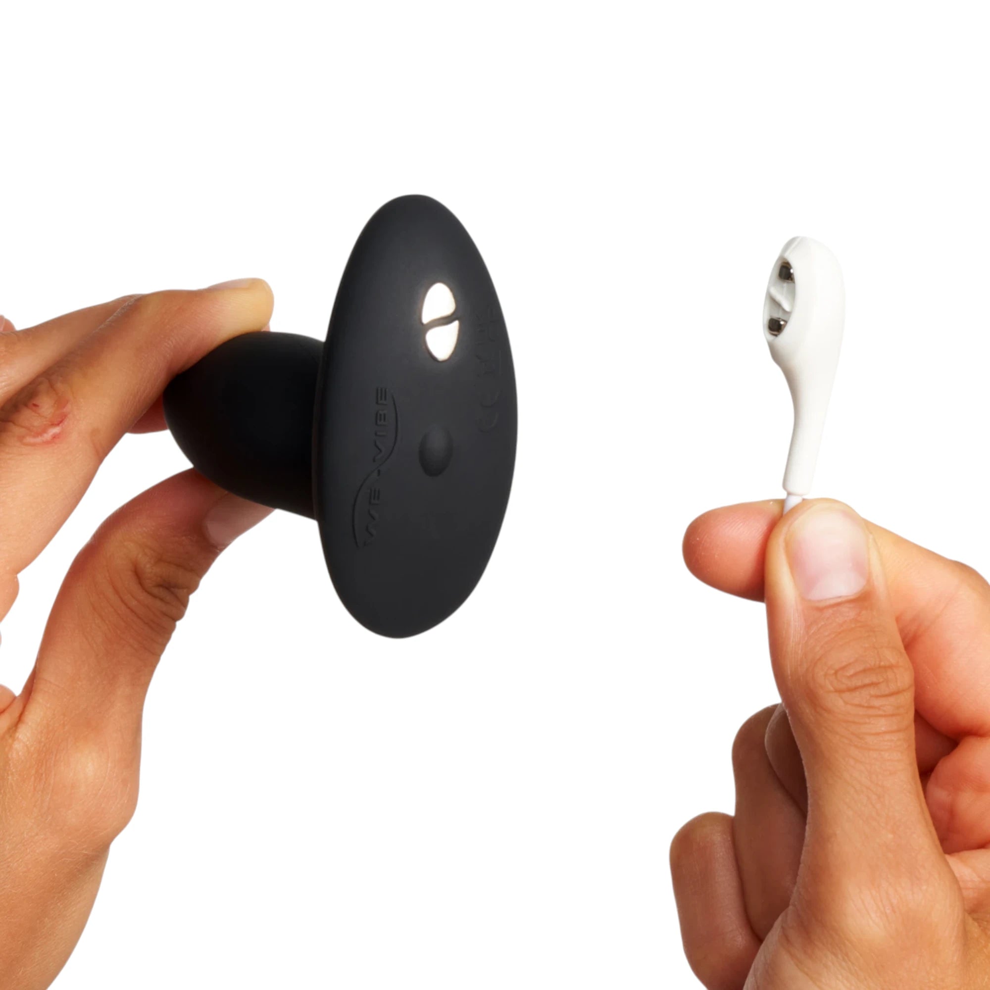 We-Vibe Ditto+ black vibrating butt plug with white wireless remote held in hands against white background