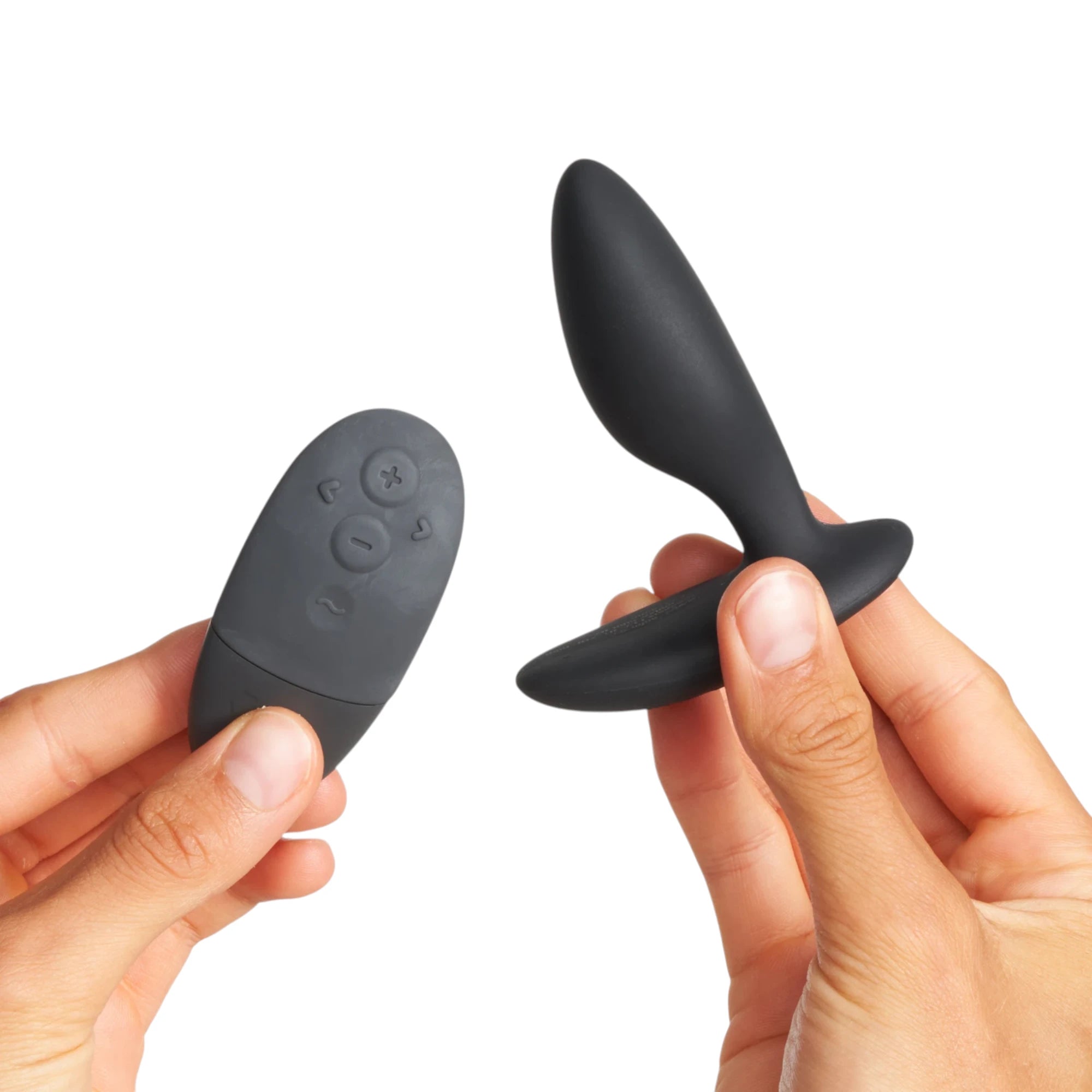 We-Vibe Ditto+ black vibrating butt plug with grey wireless remote showing control buttons held in hands against white background
