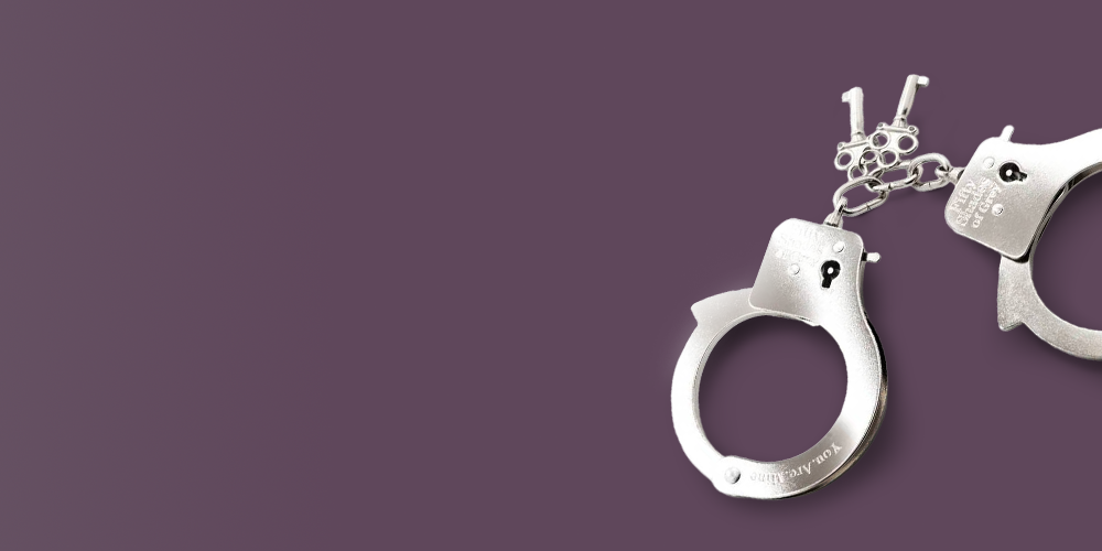 Pair of polished silver metal handcuffs with decorative chain links and engraved text on the cuffs, displayed on the right side of a deep mauve-purple background with large empty space on the left