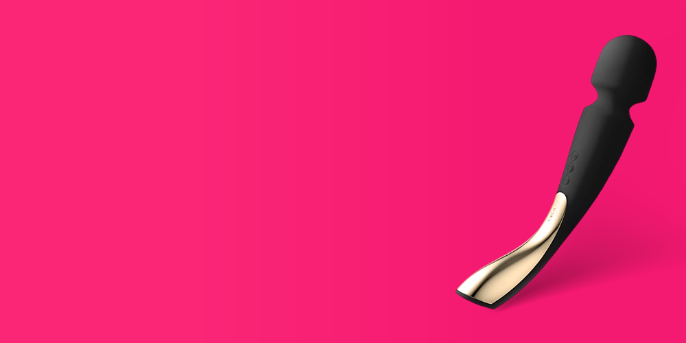 Curved wand vibrator with a matte black silicone head and neck, and a metallic gold-toned flat base, positioned diagonally on the right side of a bright hot pink background with large empty space on the left
